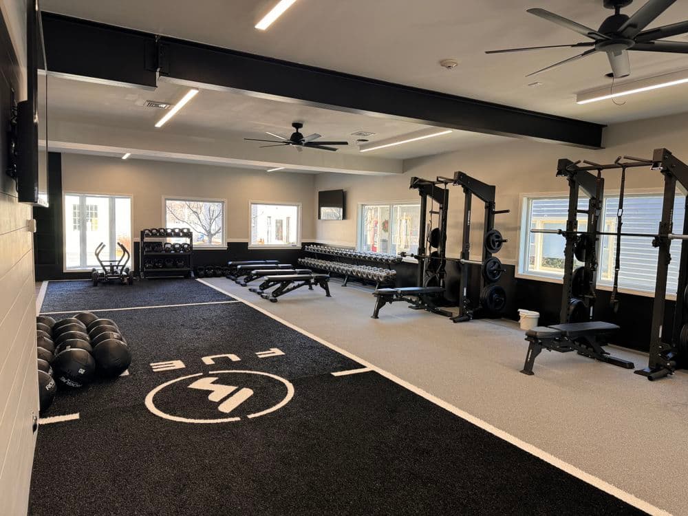 Modern gym interior featuring weights, benches, and conditioning area with ample natural light.